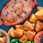 Overhead close up cider glazed bacon chops with fried potatoes, grilled tomatoes and rocket.