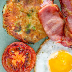 Close up overhead bubble and squeak patty with grilled tomato, fried egg and bacon.