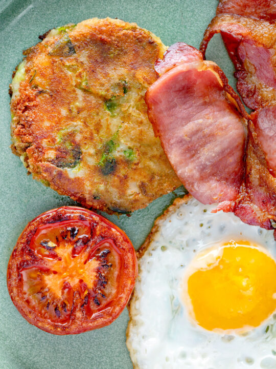 Close up overhead bubble and squeak patty with grilled tomato, fried egg and bacon.