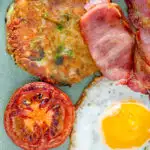 Close up overhead bubble and squeak patty with grilled tomato, fried egg and bacon featuring a title overlay.