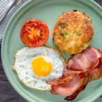 Overhead fried bubble and squeak served with bacon, grilled tomato and fried egg.
