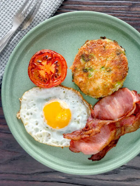 Overhead fried bubble and squeak served with bacon, grilled tomato and fried egg.