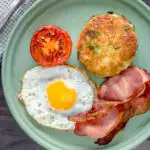 Overhead fried bubble and squeak served with bacon, grilled tomato and fried egg featuring a title overlay.