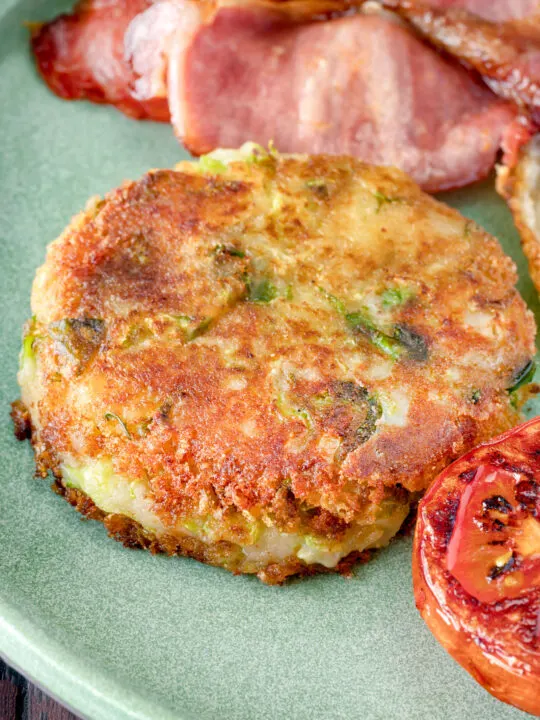 Close up fried bubble and squeak patty served with bacon, grilled tomato and fried egg.