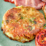Close up fried bubble and squeak patty served with bacon, grilled tomato and fried egg featuring a title overlay.