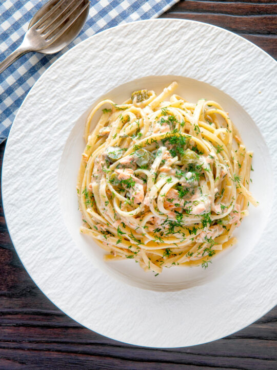 Overhead canned salmon linguini pasta with creme fraiche and cornichons.