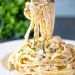 Canned salmon pasta with linguini, creme fraiche and cornichons on a fork.