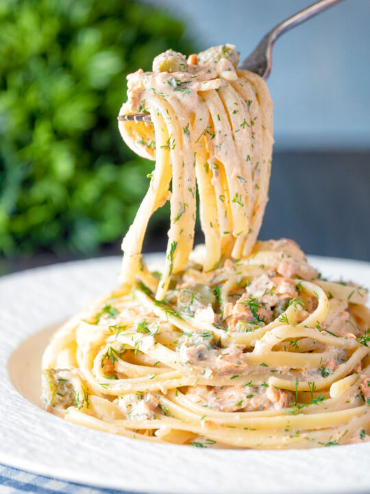 Canned salmon pasta with linguini, creme fraiche and cornichons on a fork.