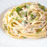 Canned salmon pasta with creme fraiche, cornichons and fresh dill served on a white plate.