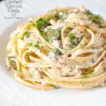 Canned salmon pasta with creme fraiche, cornichons and fresh dill served on a white plate featuring a title overlay.