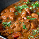 Close up chicken balti curry served in and iron karahi with fresh coriander.