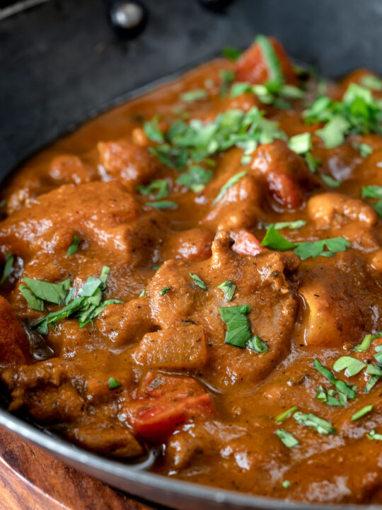 Close up chicken balti curry served in and iron karahi with fresh coriander.