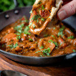 Chicken balti curry served in and iron karahi being eaten with naan bread.