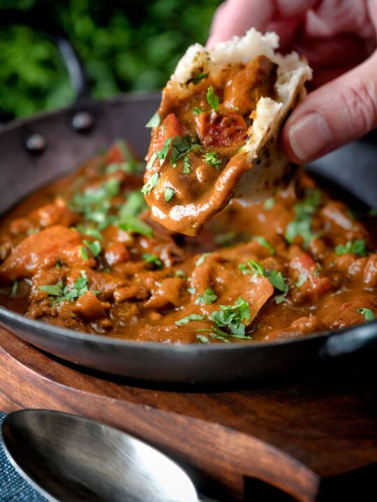 Chicken balti curry served in and iron karahi being eaten with naan bread.