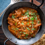 Overhead Chicken balti curry served in and iron karahi and a naan bread.
