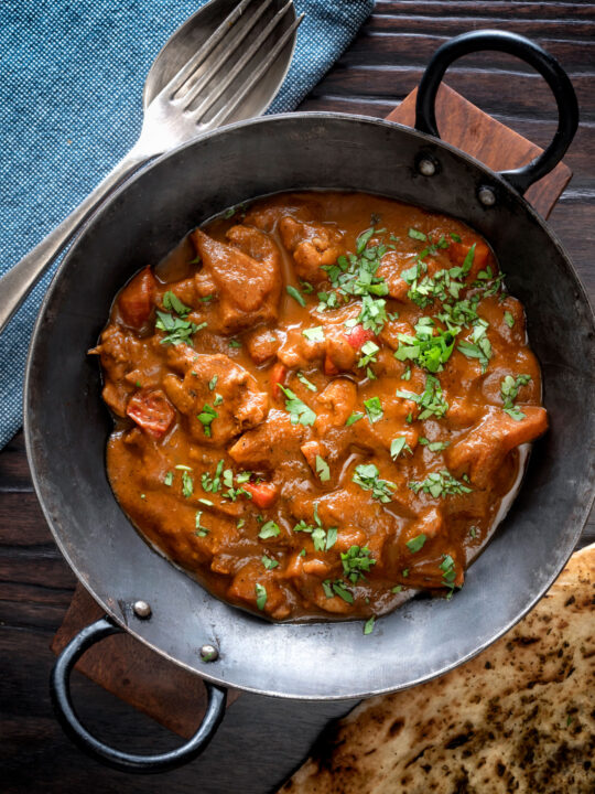 Overhead Chicken balti curry served in and iron karahi and a naan bread.