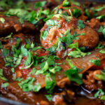 Clos up British Indian chicken jalfrezi curry with fresh coriander served in an iron karai featuring a title overlay.