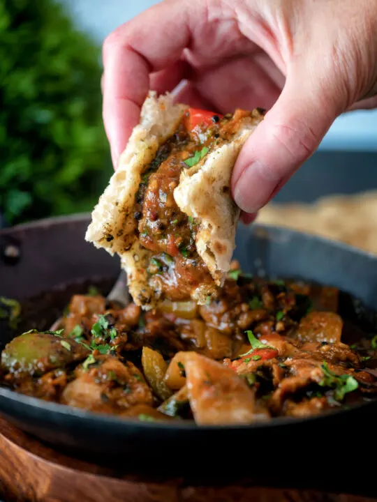 British Indian chicken jalfrezi curry being scooped up with a tandoori naan bread.