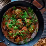 Overhead British Indian chicken jalfrezi curry with fresh coriander served in an iron karai featuring title overlay.