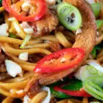 Close up chicken satay stir fry with peanuts and egg noodles featuring a title overlay.