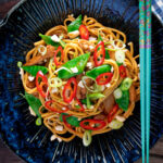 Overhead chicken satay stir fry with peanuts and egg noodles featuring a title overlay.