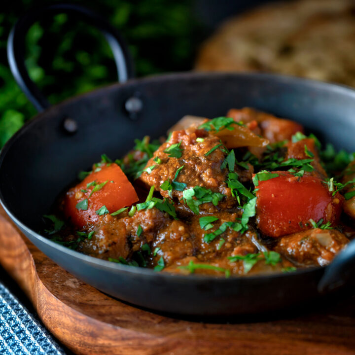 Indian influenced lamb jalfrezi curry served in an iron karahi with a naan bread.