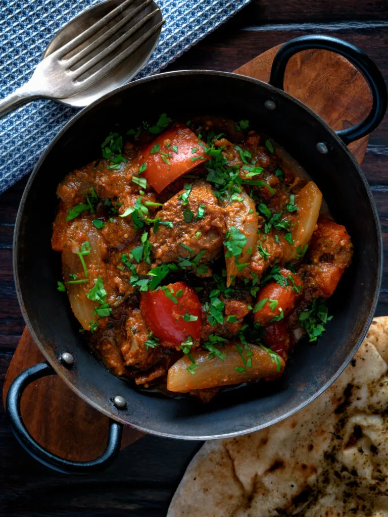 Overhead Indian influenced lamb jalfrezi curry served with a naan bread.