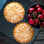 Overhead mini Bakewell tarts with a frangipane filling and almond topping featuring a title overlay.