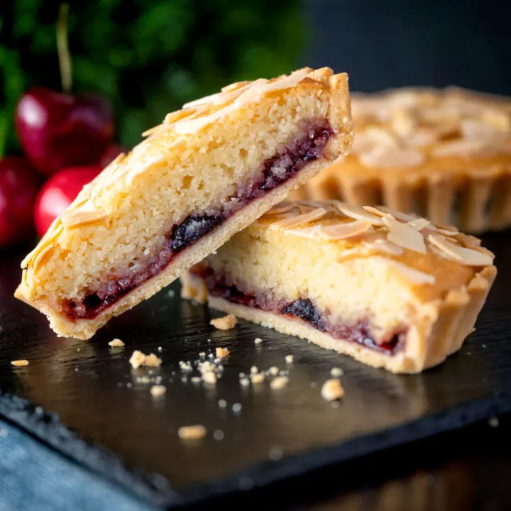 Mini Bakewell tarts with a sweet crust pastry cut open to show frangipane & jam filling.