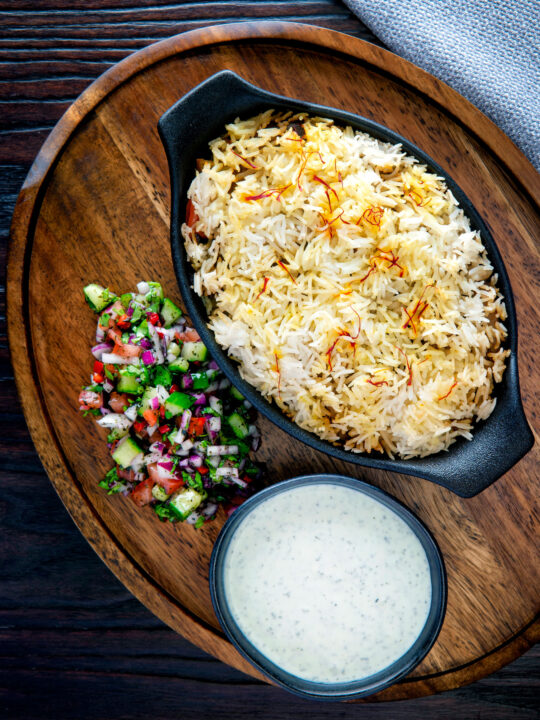 Overhead vegan mushroom biryani served with raita and kachumber salad.