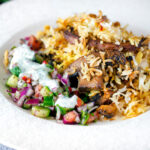 Vegan mushroom biryani served with raita and kachumber salad on a plate.