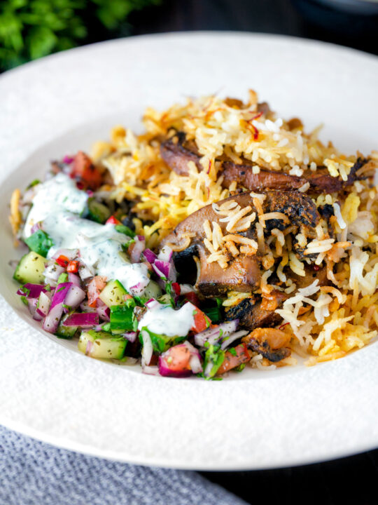 Vegan mushroom biryani served with raita and kachumber salad on a plate.