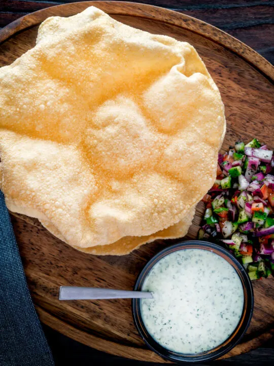 Overhead Indian poppadoms or papad served with kachumber salad and mint raita.