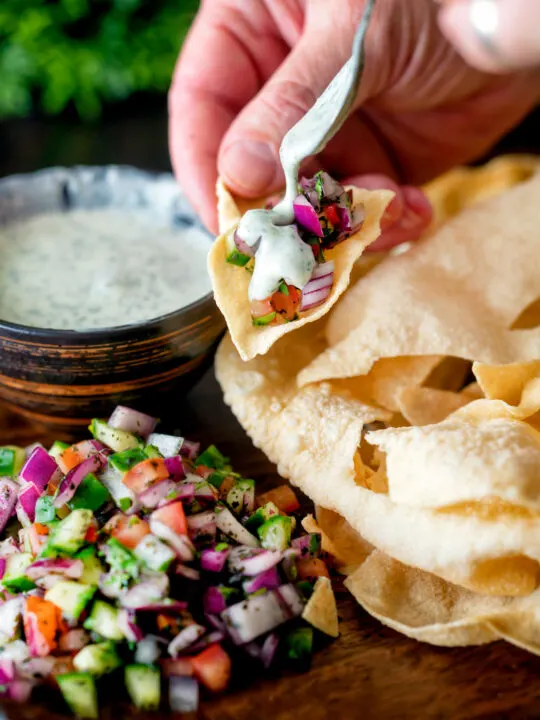 Indian poppadoms being topped with kachumber salad and a mint & yoghurt raita.