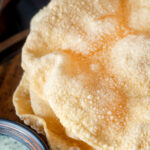 Close up freshly cooked poppadoms or papad served with mint raita featuring a title overlay.