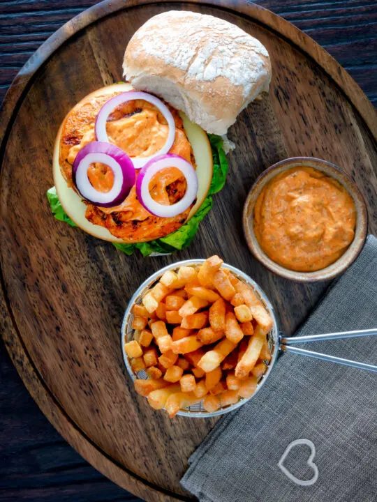 Overhead peri peri chicken burger served with spicy mayonnaise and French fries.