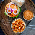 Overhead peri peri chicken burger served with spicy mayonnaise and French fries featuring a title overlay.