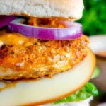 Close up peri peri chicken burger served with red onion and smoked cheese.