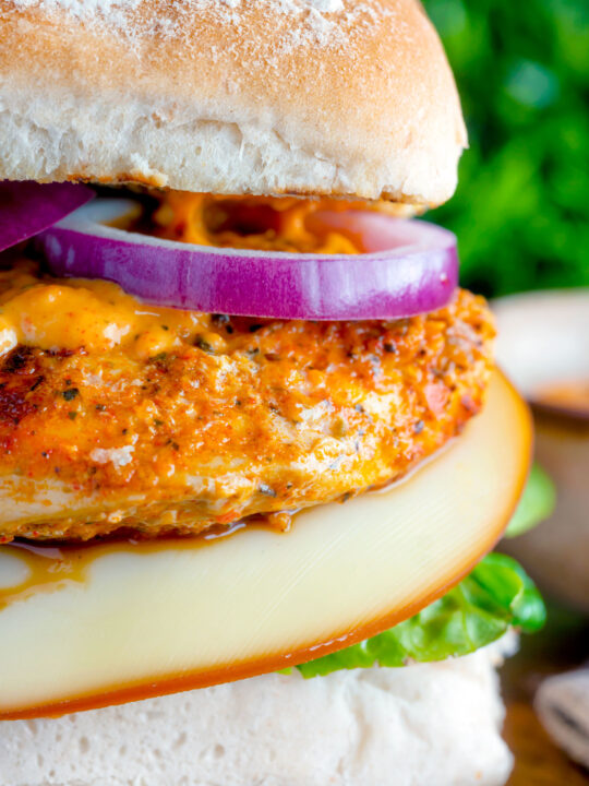 Close up peri peri chicken burger served with red onion and smoked cheese.