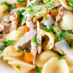Close up braised rabbit ragu served with orecchiette pasta and fresh parsley.