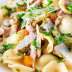Close up braised rabbit ragu served with orecchiette pasta and fresh parsley featuring a title overlay.