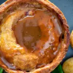 Close up traditional Scotch meat pie served with lamb gravy.