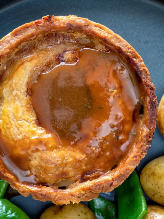 Close up traditional Scotch meat pie served with lamb gravy.