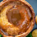 Close up traditional Scotch meat pie served with lamb gravy featuring a title overlay.