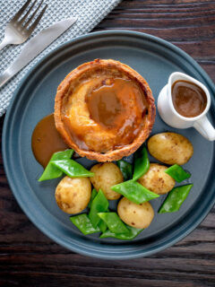 Overhead traditional Scotch meat pie served with lamb gravy, potatoes and runner beans.