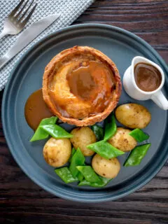 Overhead traditional Scotch meat pie served with lamb gravy, potatoes and runner beans.