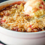Close up individual strawberry crumble with balsamic vinegar served with vanilla ice cream.