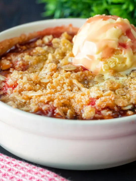 Close up individual strawberry crumble with balsamic vinegar served with vanilla ice cream.