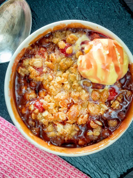 Overhead individual strawberry crumble with balsamic vinegar served with vanilla ice cream.