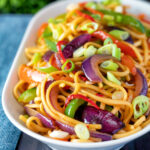 Stir fried sweet chilli noodles with peppers, red onions garnished with spring onion.